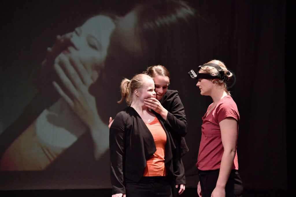 Drie dansers van Misiconi staan op het podium en spelen het stuk Flirt Fantasies. Een van de dansers heeft een GoPro op haar hoofd, het beeld hiervan wordt achter de dansers geprojecteerd.