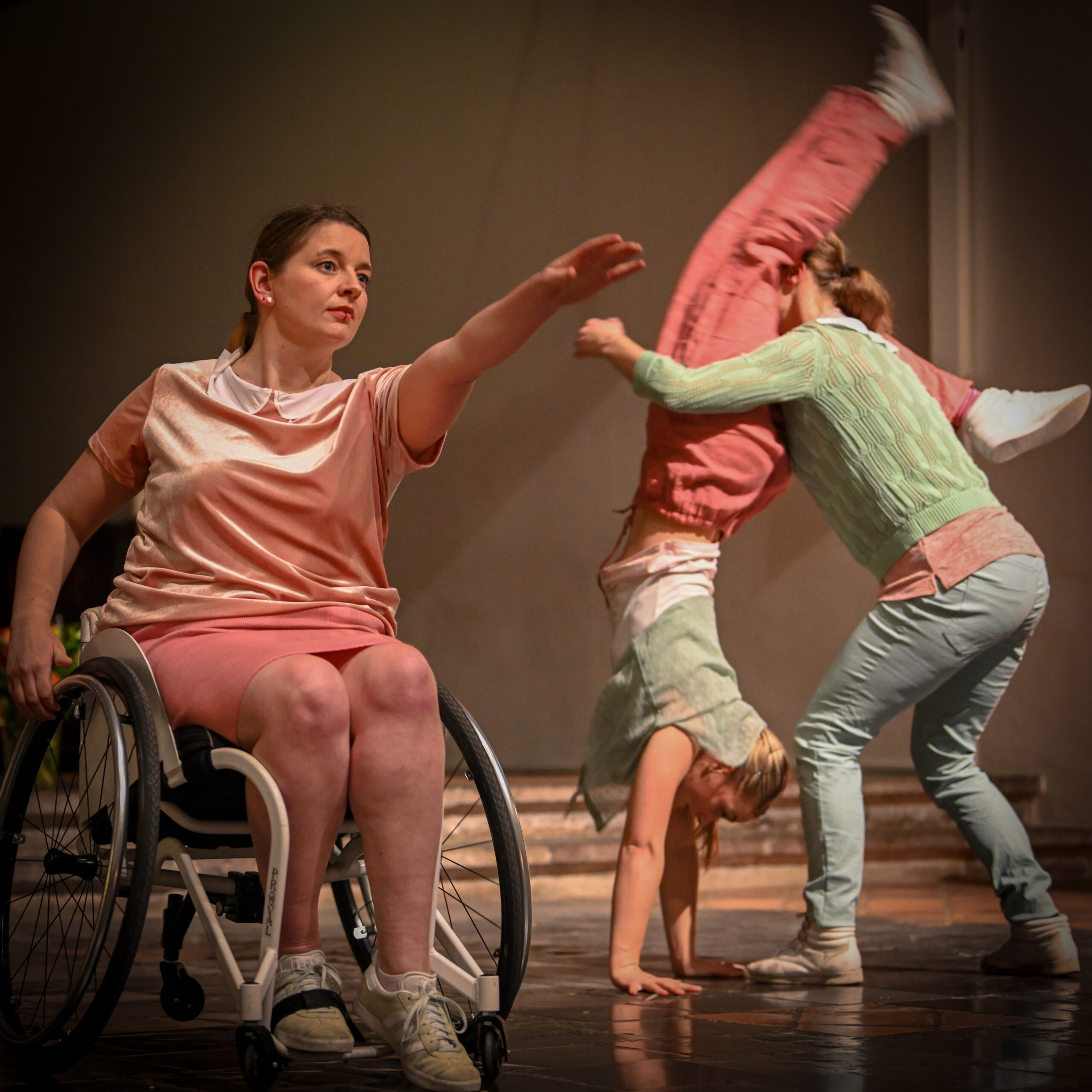 Drie dansers van Misiconi op een podium. Jacqueline van Kuilenburg zit in een rolstoel en een andere dansers staat op haar handen.
