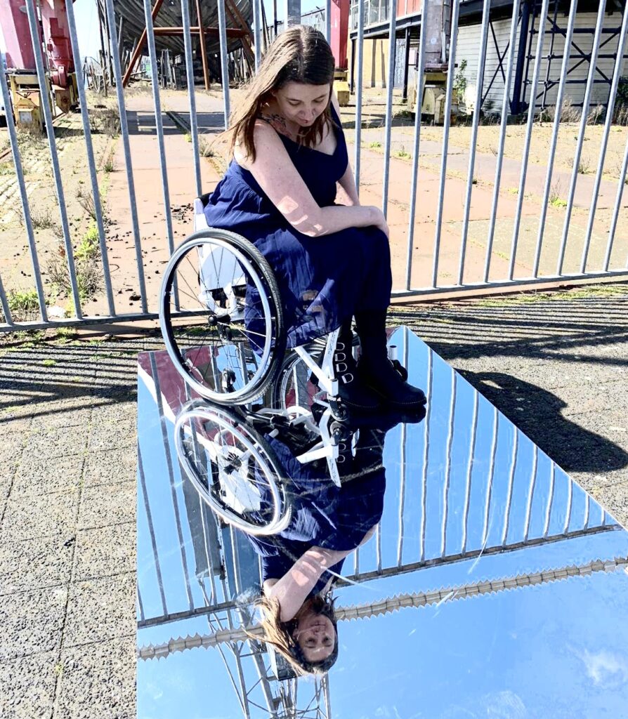 Danser Jacqueline zit in een rolstoel die op een spiegel staat.