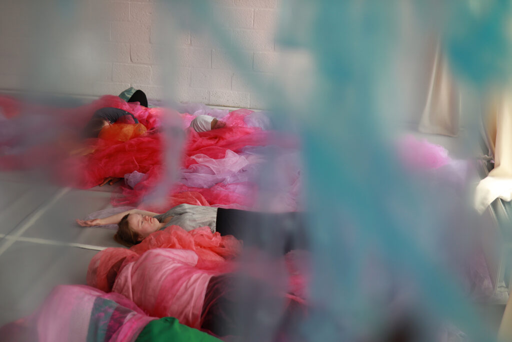 De dansers van Misiconi liggen in felgekleurde doeken op de grond voor de voorstelling TIDES